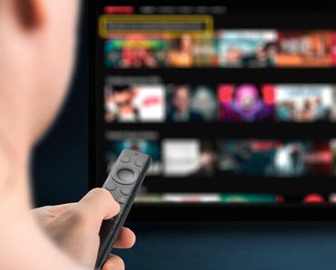 A person points a remote at a smart TV and chooses a streaming show or movie to watch.