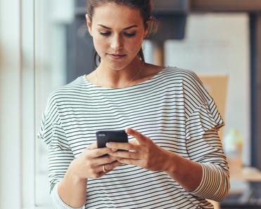 A woman leans against a doorframe while she uses a smartphone