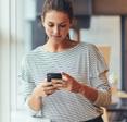 A woman leans against a doorframe while she uses a smartphone