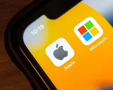A close-up of a smartphone screen showing the logo for Apple next to the logo for Microsoft to represent Mac vs. PC.
