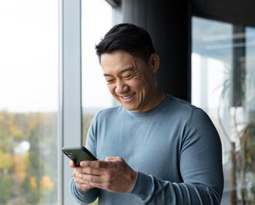 Asian man smiling down at cellphone screen