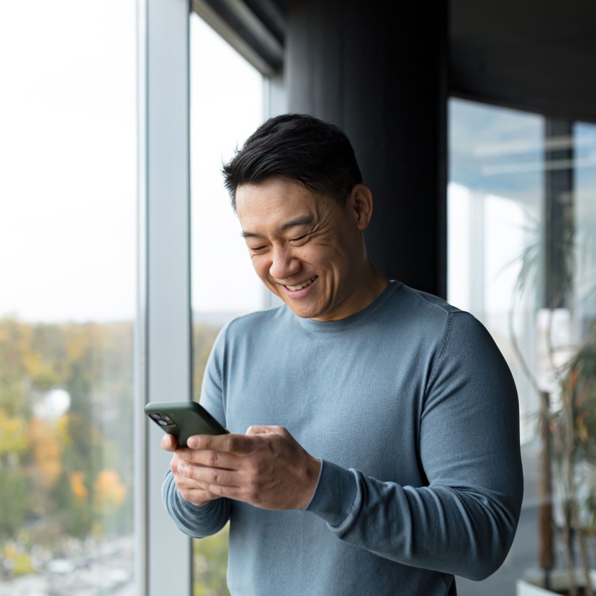 Asian man smiling down at cellphone screen