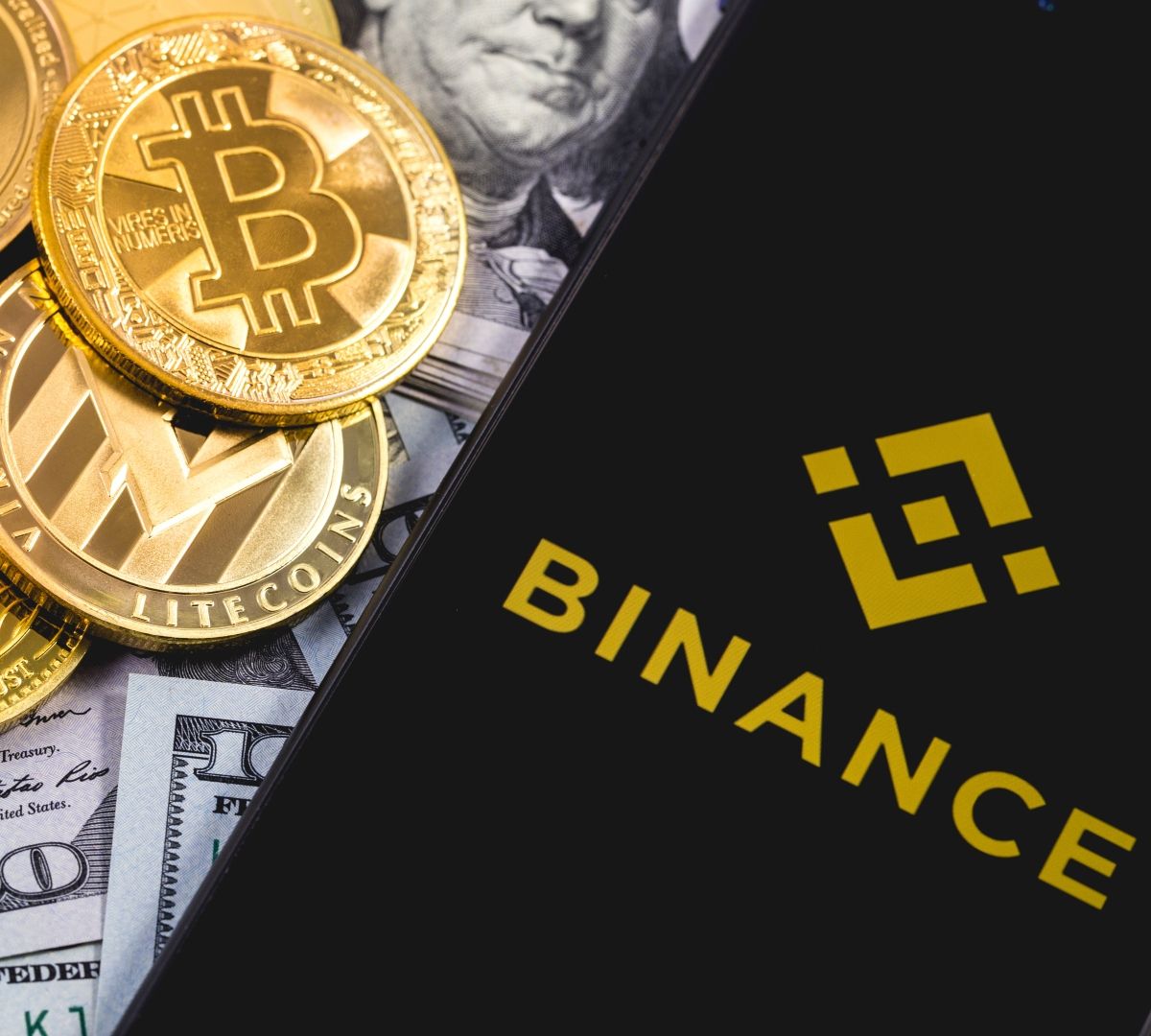 bills, cryptocurrency gold coins, and cellphone on top with Binance on the screen