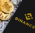 bills, cryptocurrency gold coins, and cellphone on top with Binance on the screen