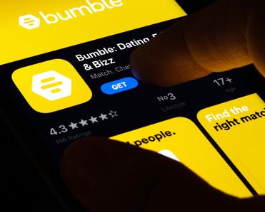 Phone screen with dating app Bumble in yellow and finger about to press the button get