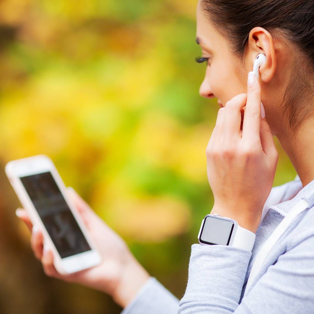 A woman touching her Bluetooth earpod and holding her smartphone.