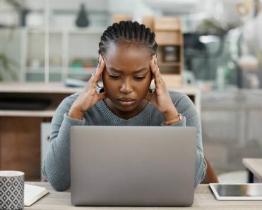 A woman working on her laptop and looking stressed out.