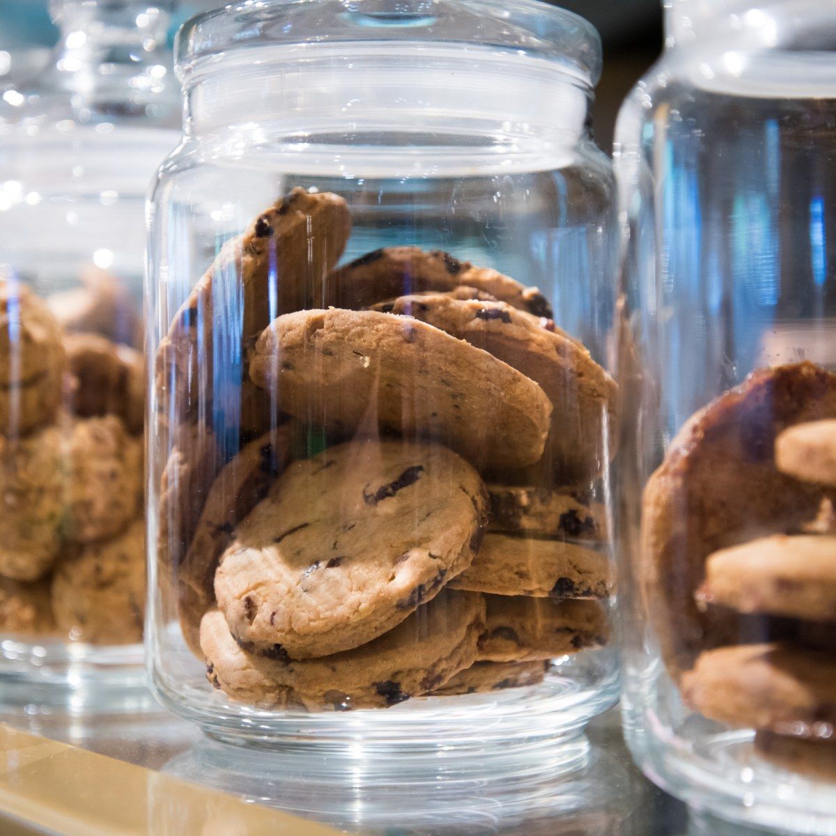 A close up of several chocolate chip cookies in a clear glass jar.