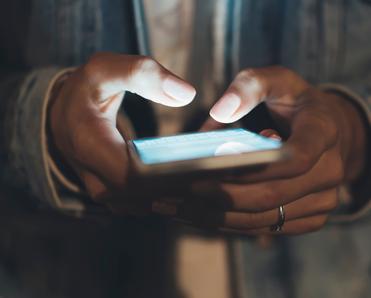 A close-up of a woman&#x27;s hands illuminated by her smartphone screen as she types.