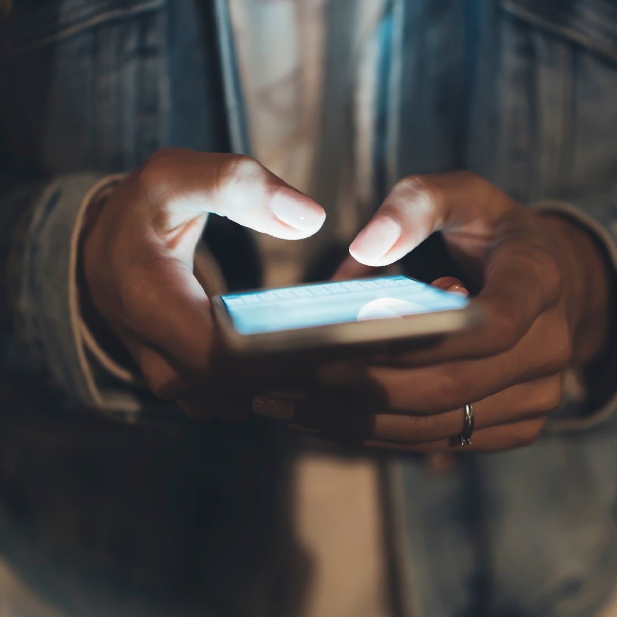 A close-up of a woman&#x27;s hands illuminated by her smartphone screen as she types.