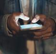 A close-up of a woman&#x27;s hands illuminated by her smartphone screen as she types.