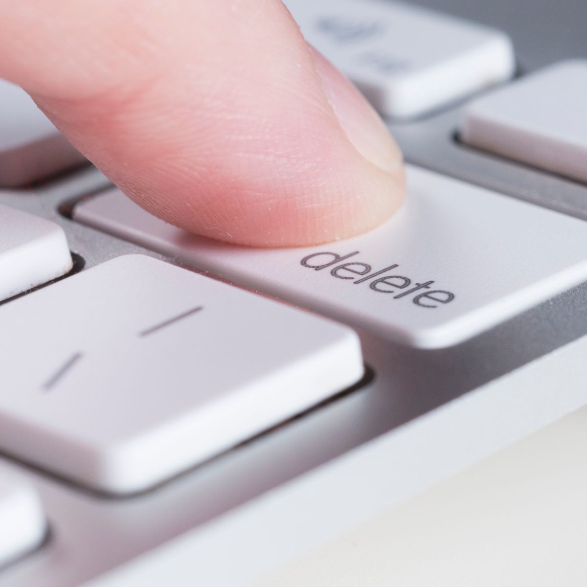 A close-up of a finger pressing a white delete button on a Mac keyboard.