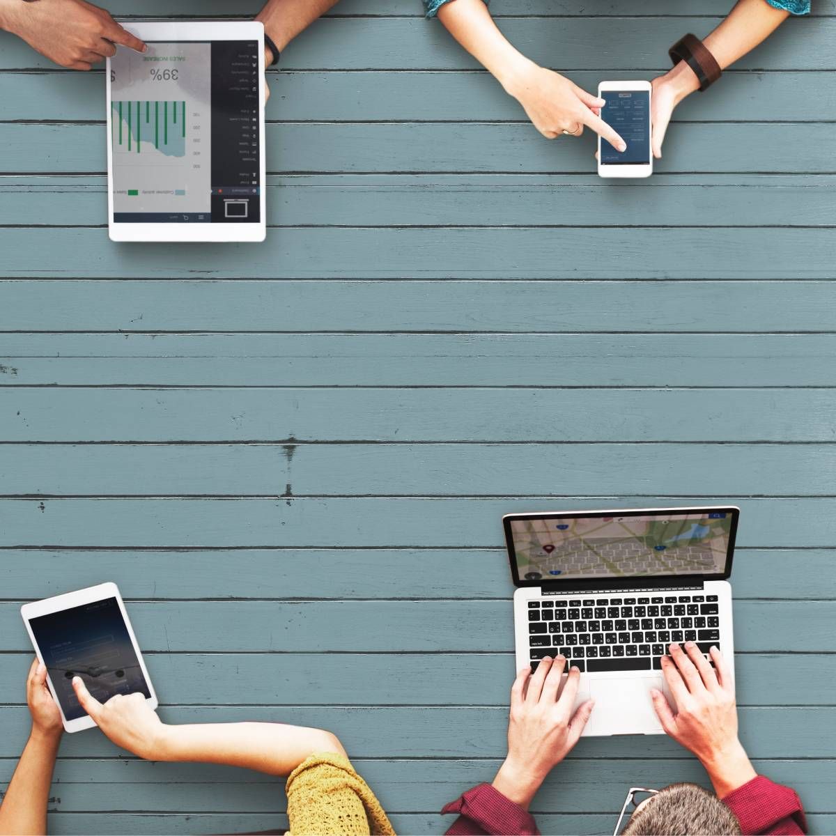 A group of people are seated at a table using different electronic devices, including a tablet, a smartphone, and a laptop, and they are all connected to the internet.