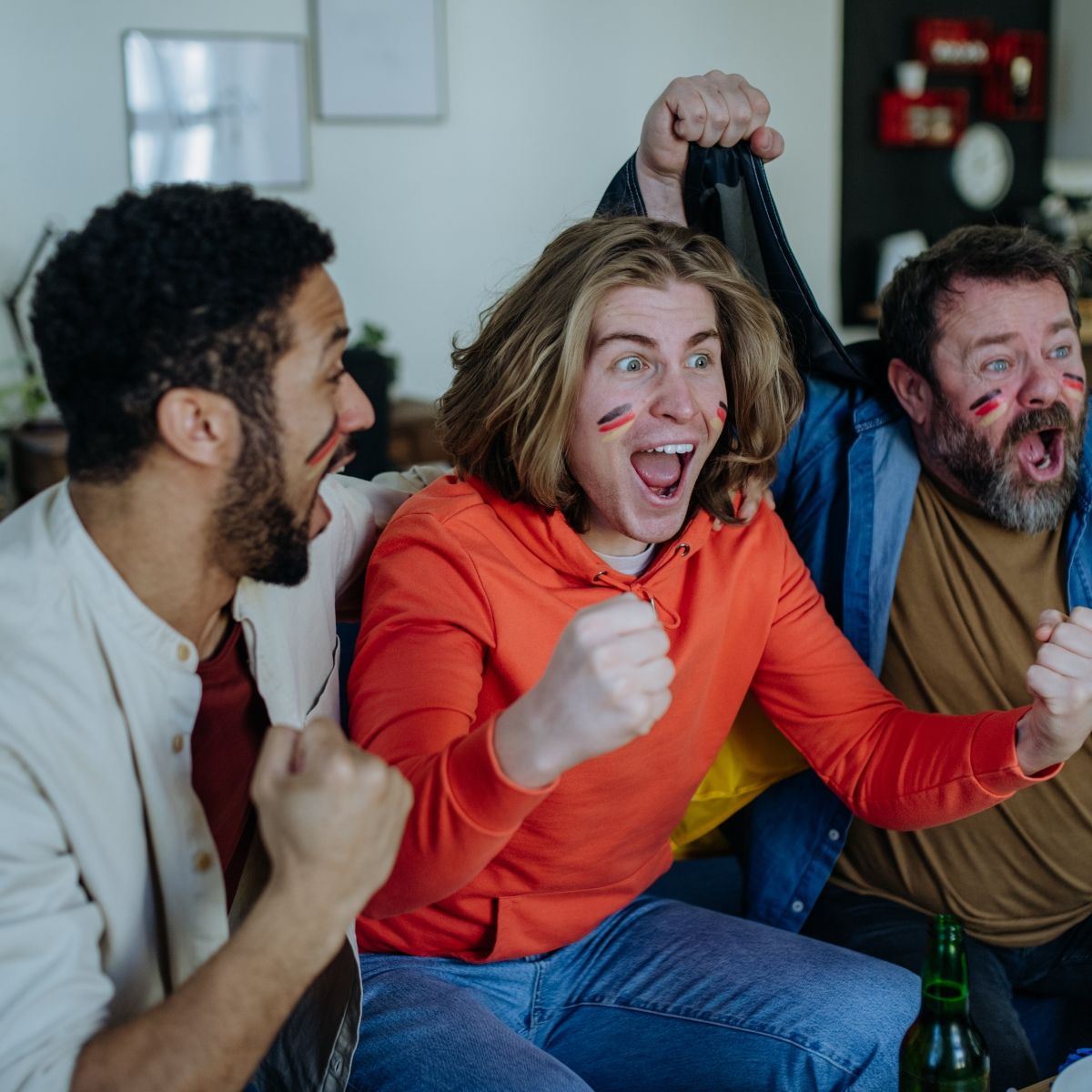 three man with German flag paint on their faces cheering for soccer game