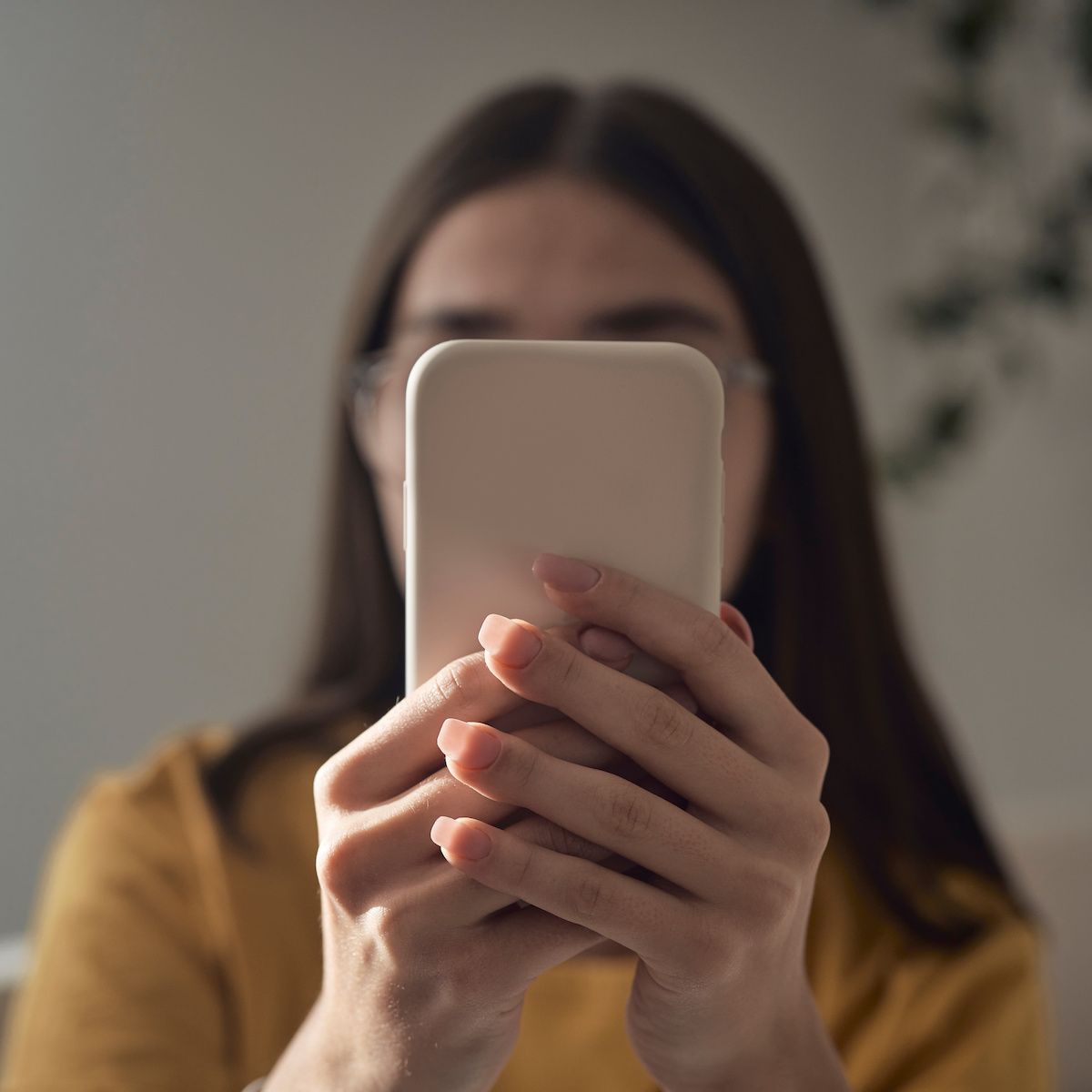 A teenage girl with brown hair holds a phone up to hide her face representing anonymous calls and texts.
