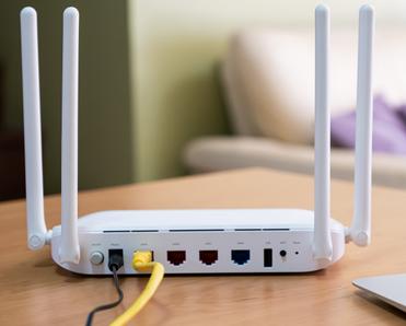 A white wireless router sits on a wood table in a living room. Rebooting your router every so often is a good idea to keep your connection secure.