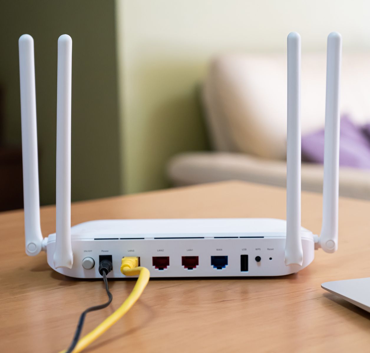 A white wireless router sits on a wood table in a living room. Rebooting your router every so often is a good idea to keep your connection secure.