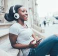 A young Black woman sits on steps outside and listens to music on Spotify.