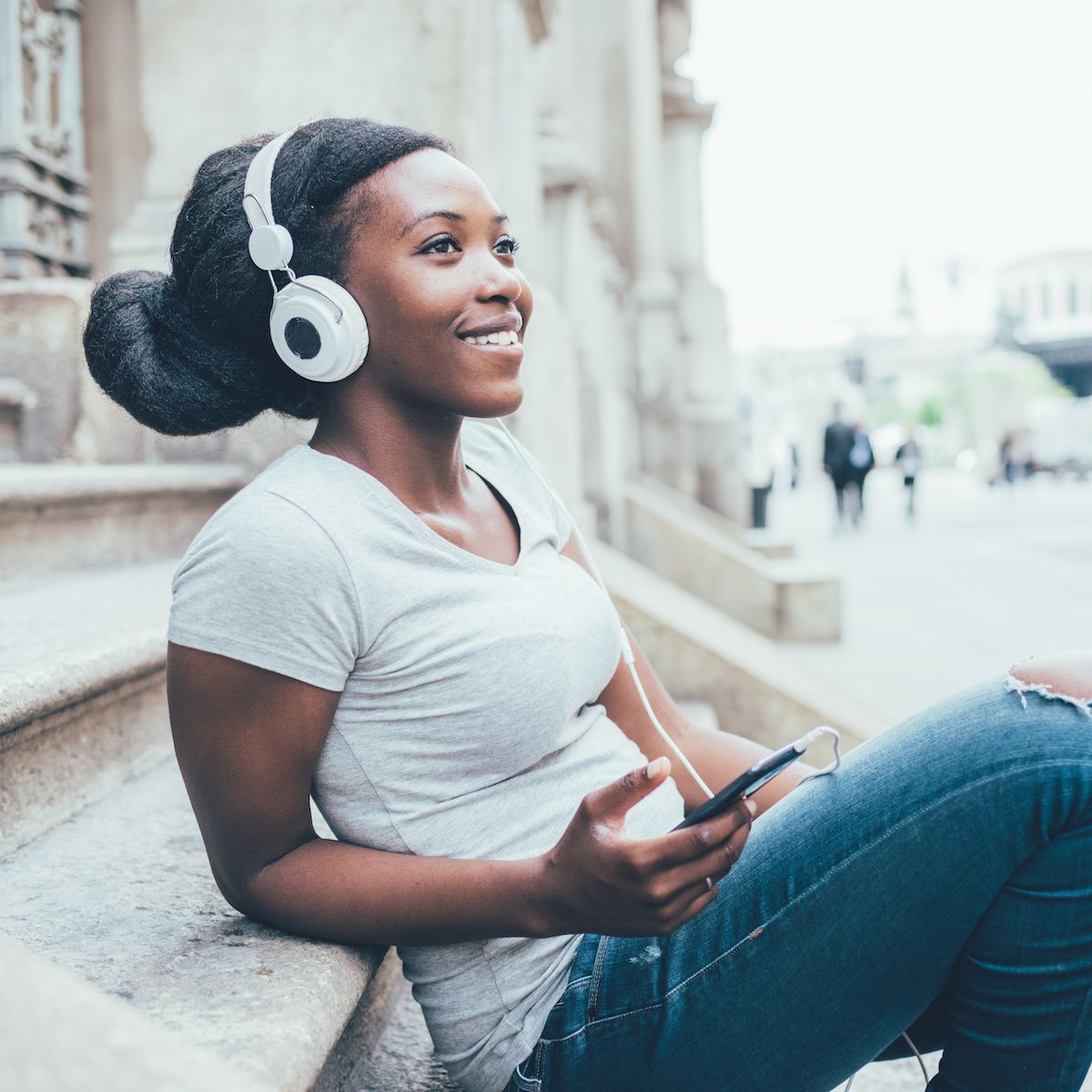A young Black woman sits on steps outside and listens to music on Spotify.