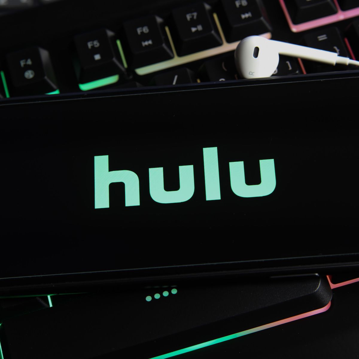 A close-up of a smartphone screen with the Hulu logo in green on a black background. The phone is sitting on top of a gaming computer keyboard.