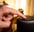 A hand pressing the voice control button on an Amazon Echo.