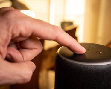 A hand pressing the voice control button on an Amazon Echo.