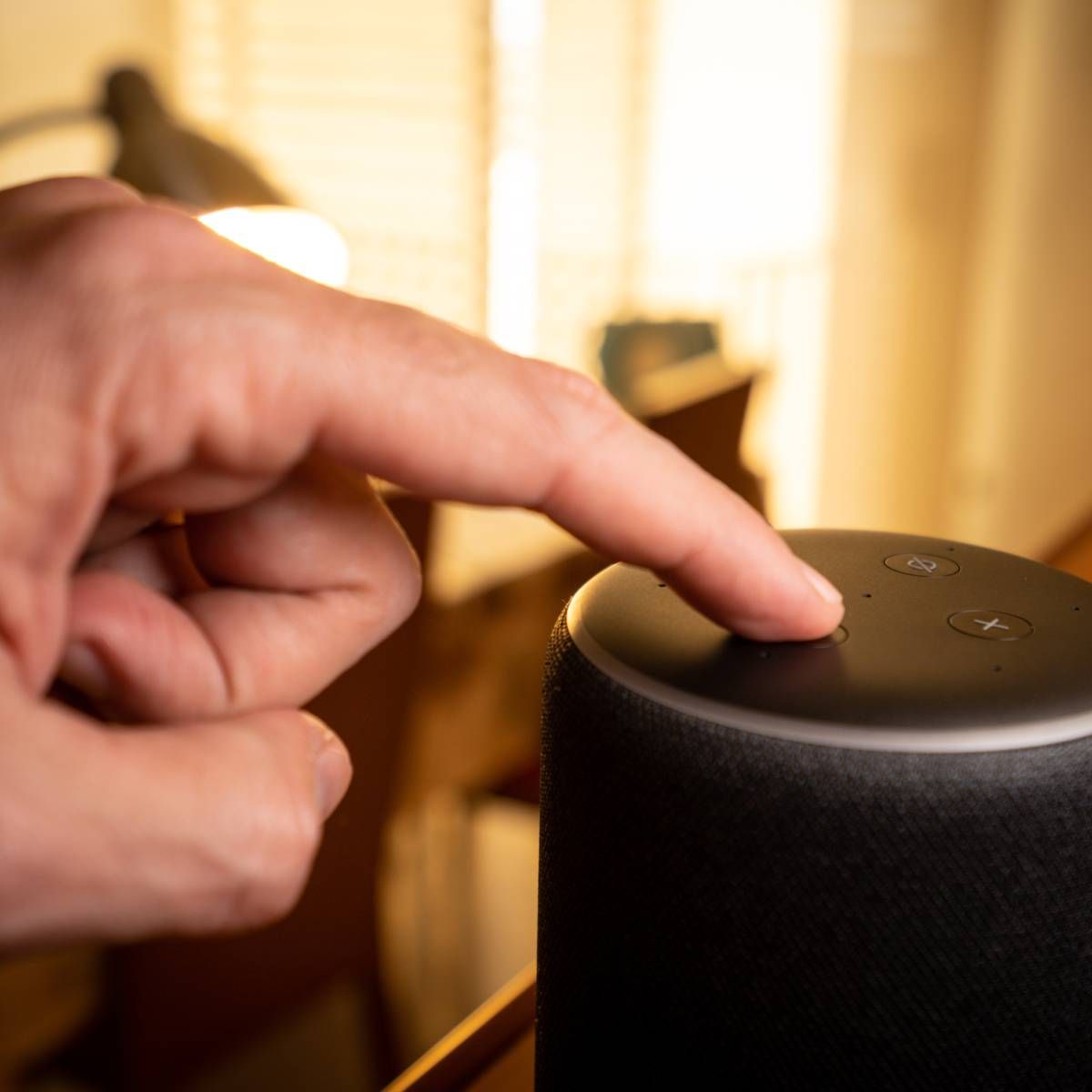 A hand pressing the voice control button on an Amazon Echo.
