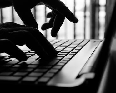 A black and white photo of backlit hands typing on a laptop keyboard to simulate someone stealing a Wi-Fi connection.