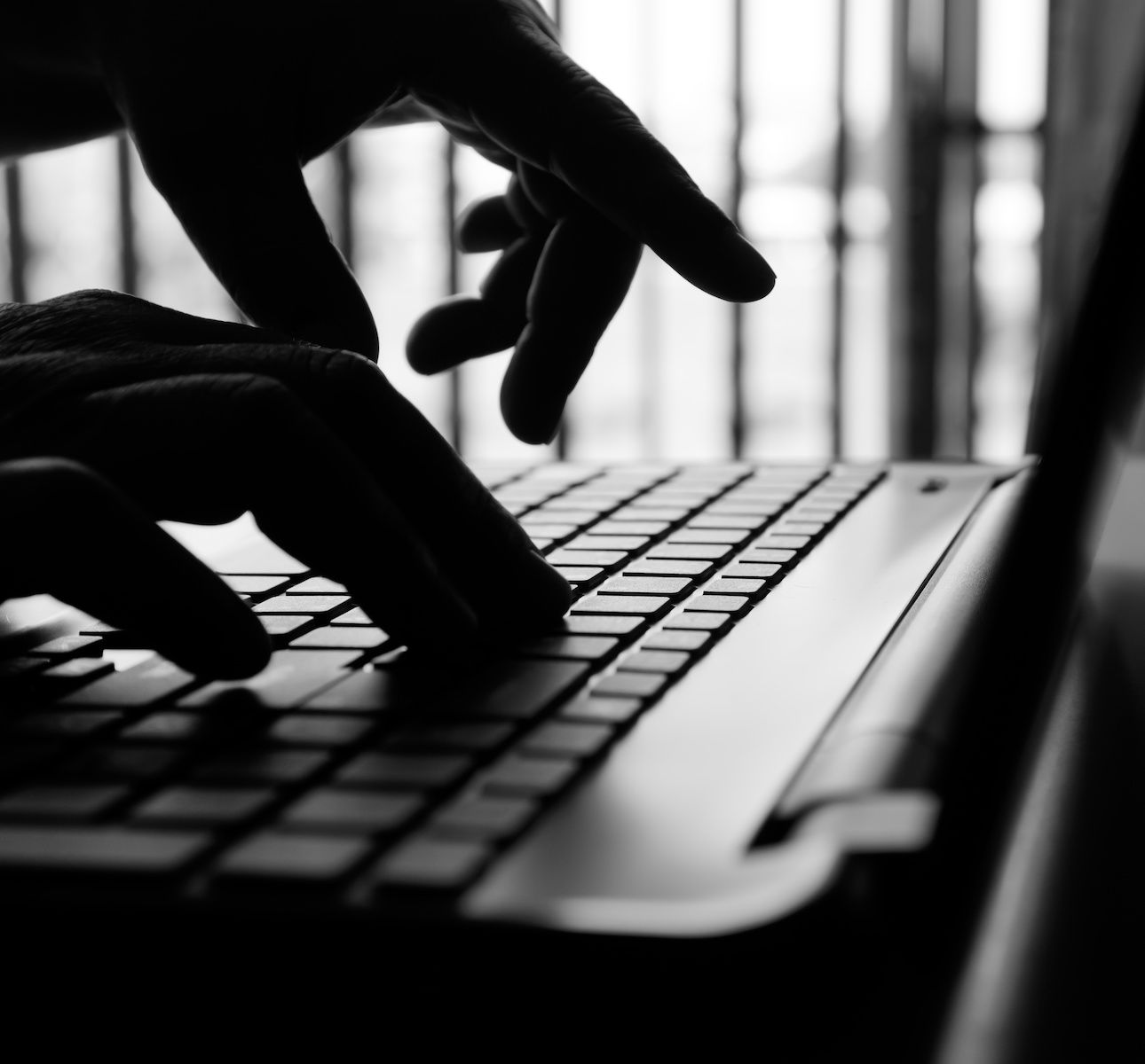 A black and white photo of backlit hands typing on a laptop keyboard to simulate someone stealing a Wi-Fi connection.