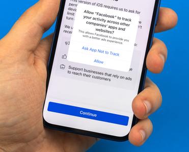 A man&#x27;s hand holds a new iPhone with a prompt to allow or not allow Facebook to track activity on the screen.