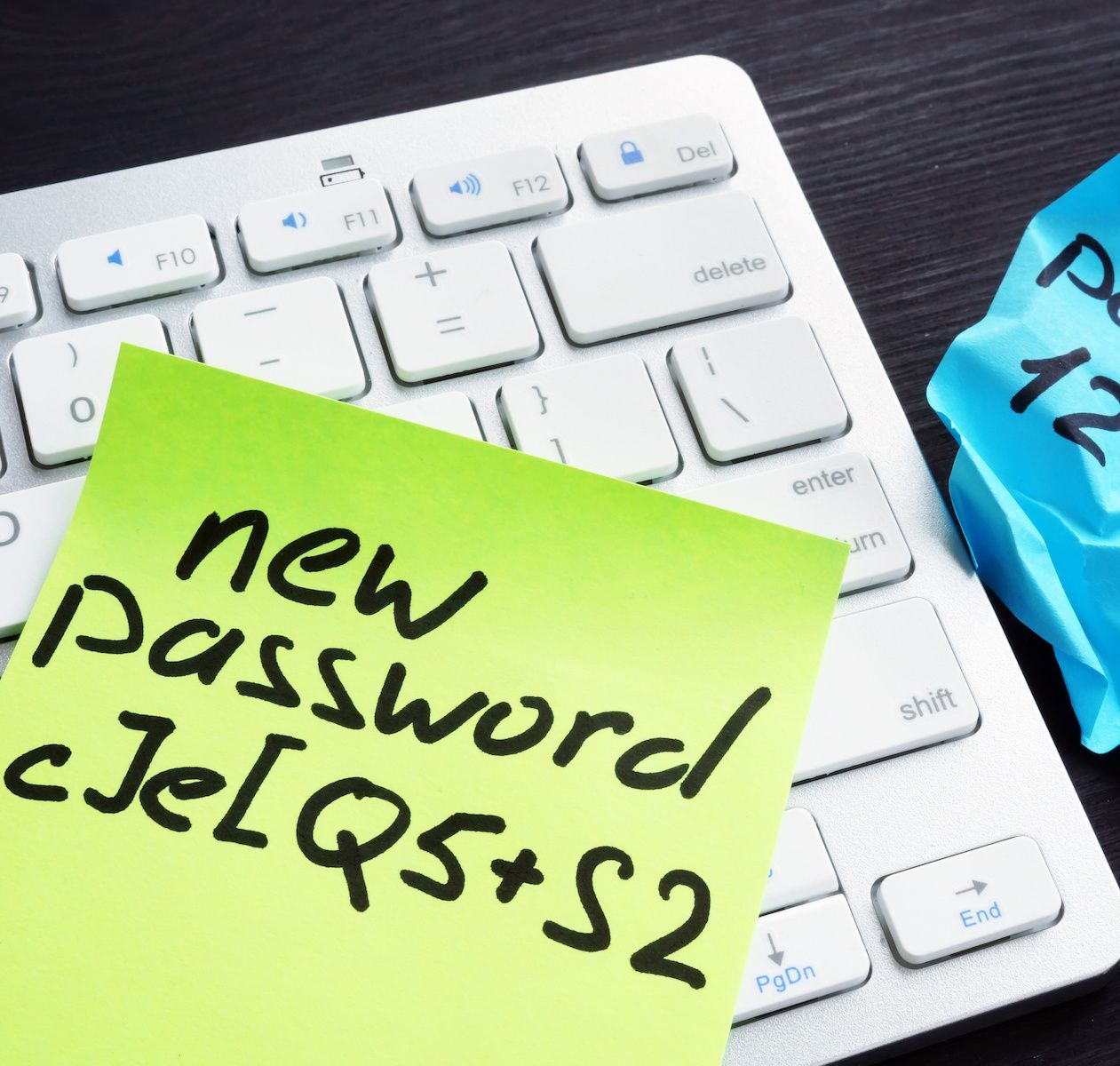 A strong password written on a yellow Post-it note sitting on top of an Apple keyboard.