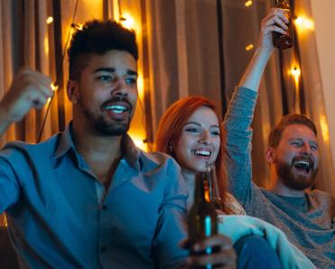 Two men and a woman cheer while they watch their favorite sports team score on the TV.