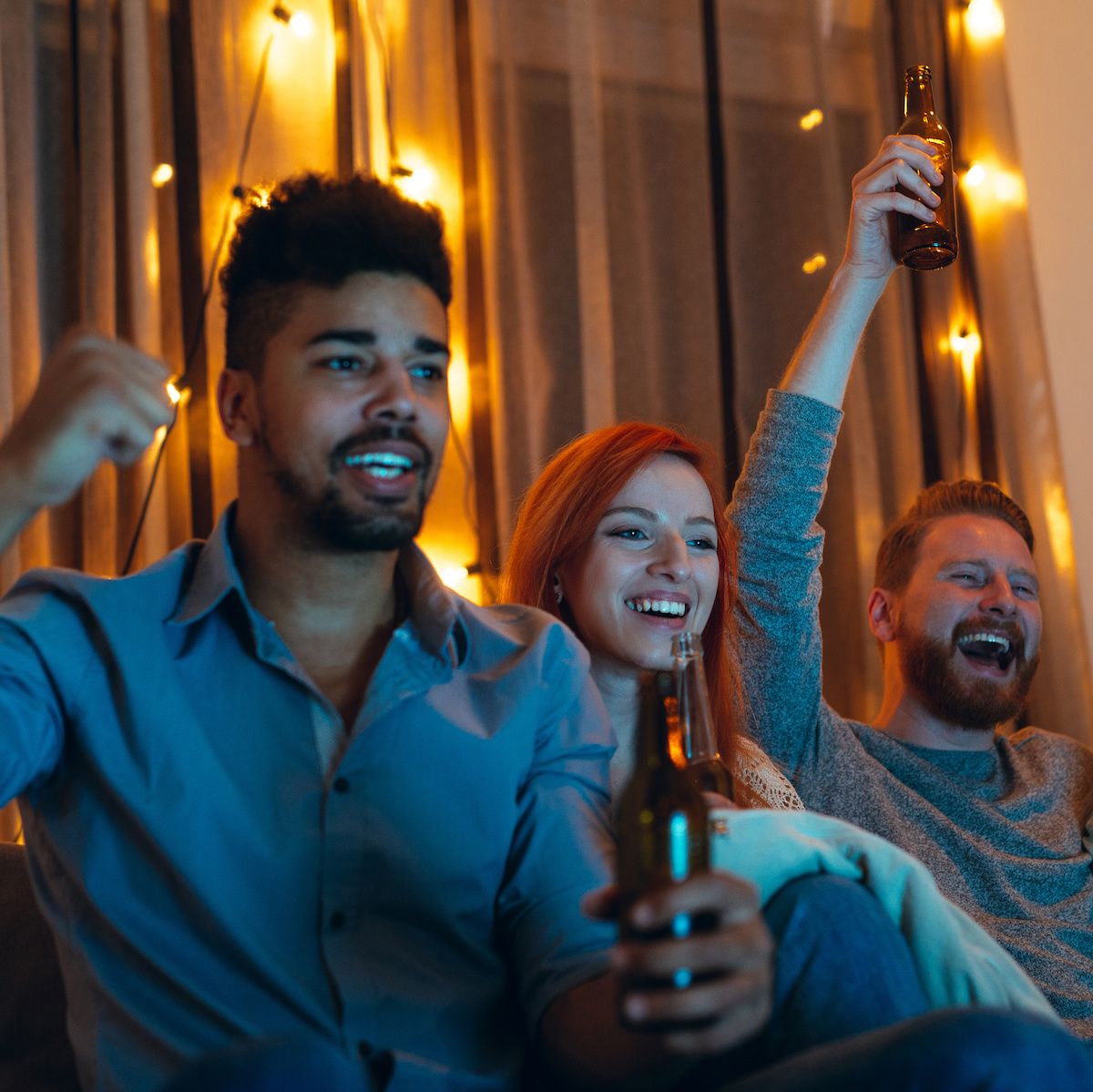 Two men and a woman cheer while they watch their favorite sports team score on the TV.