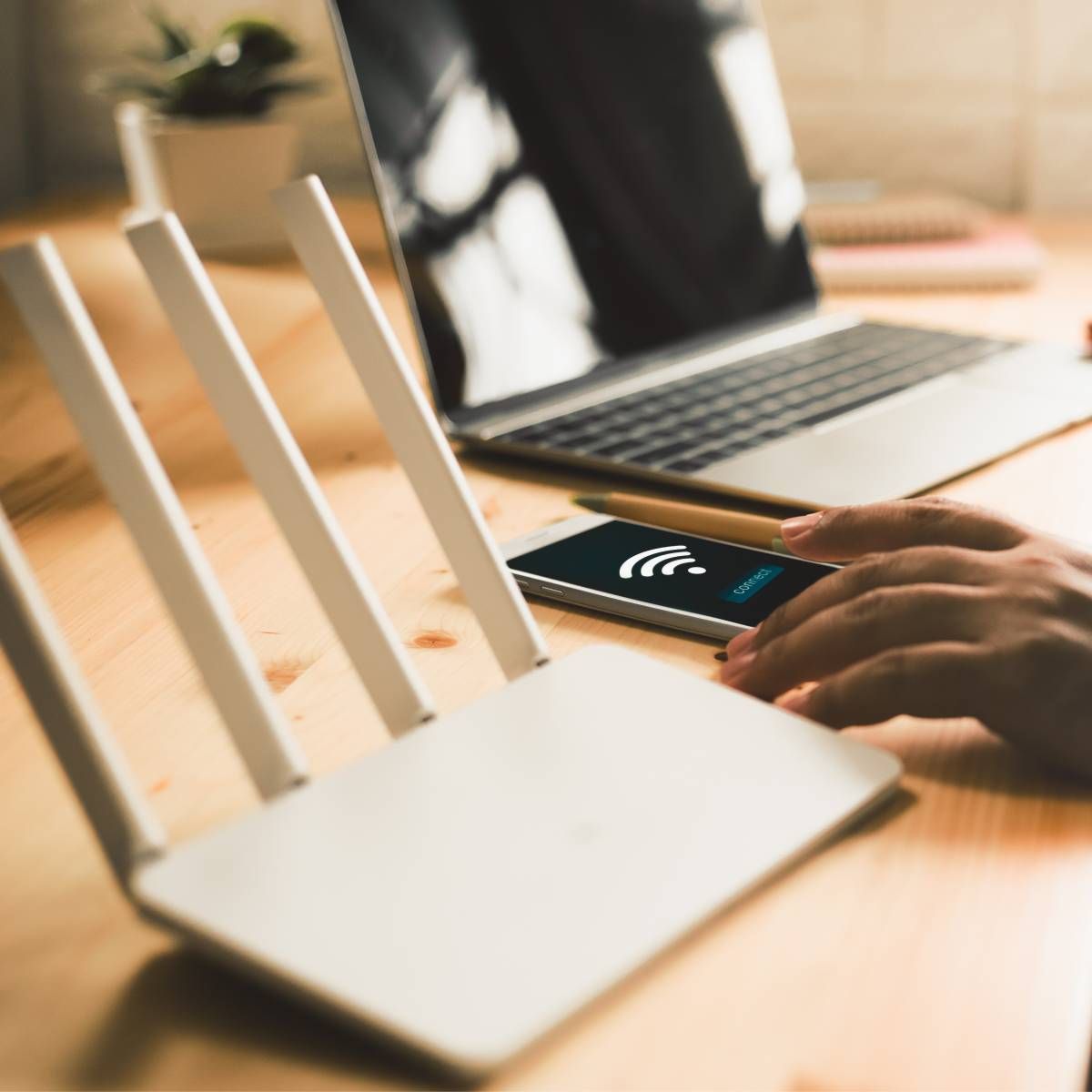 A man using his smartphone to connect to the Wi-Fi with a router and a laptop in the background.