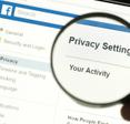 Hand holding a magnifying glass and magnifying the word &quot;Privacy settings&quot; on Facebook.