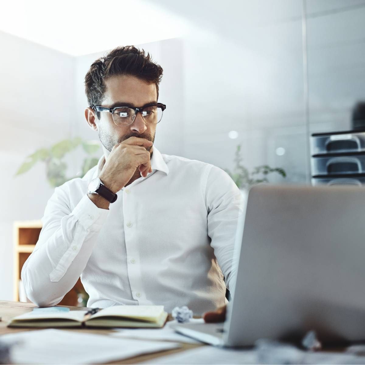 A man sitting at his desk, staring at his laptop and deep in thought. 