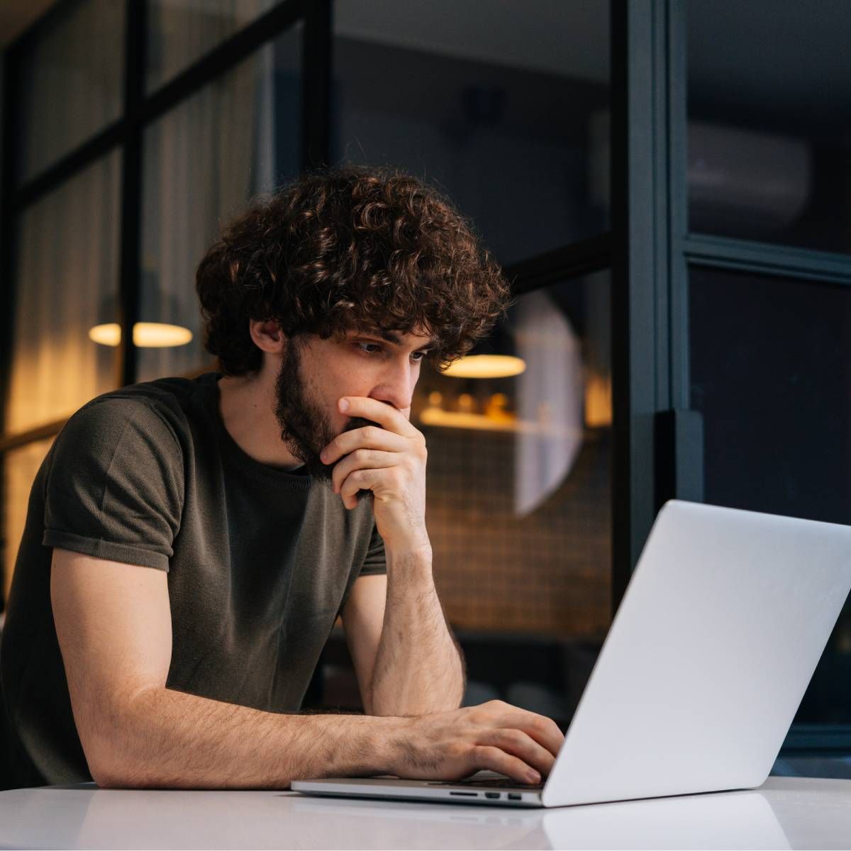 A young man sitting at his kitchen table while working on his laptop.