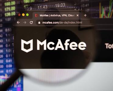 McAfee company logo on a website with blurry stock market developments in the background, seen on a computer screen through a magnifying glass.