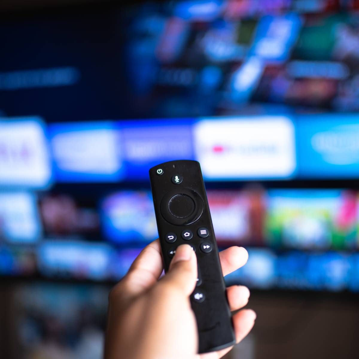 An Amazon Fire TV stick remote is being held and pointed at a TV.