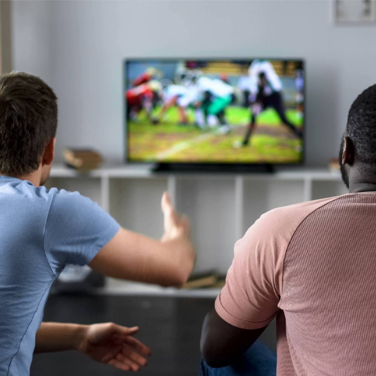 Friends gathered on a couch watching an American football game from their living room television.