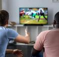 Friends gathered on a couch watching an American football game from their living room television.