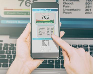 A man&#x27;s hands hold up a cell phone that shows a 765 credit score, intended to show the idea of credit monitoring and how it&#x27;s important to noticing and protecting yourself against identity theft.