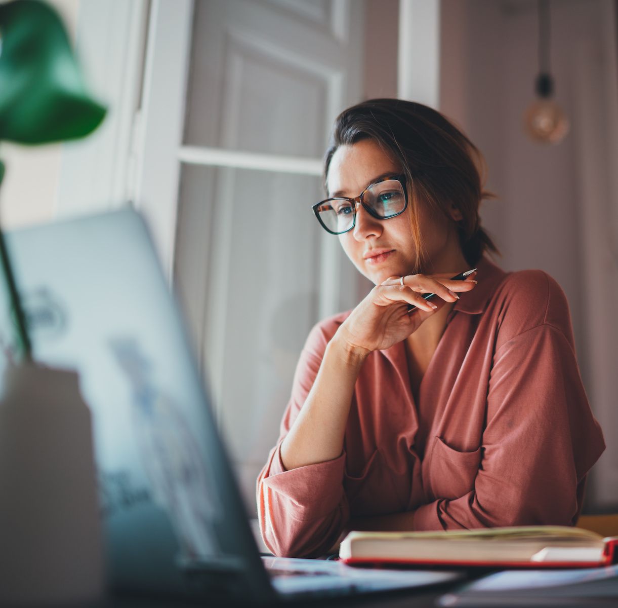 A woman sits at her desk and looks at her laptop. If she&#x27;s using public Wi-Fi, she should check to make sure her VPN is working.