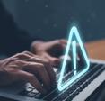 man&#x27;s hands typing on laptop keyboard and a triangle exclamation warning sign floating above