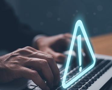 man&#x27;s hands typing on laptop keyboard and a triangle exclamation warning sign floating above