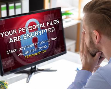 A man looks scared as he stares at his computer monitor, which shows a ransomware attack message