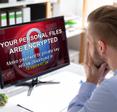 A man looks scared as he stares at his computer monitor, which shows a ransomware attack message