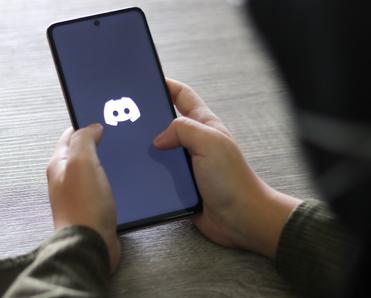 A close-up view of a woman holding a cell phone with the Discord app logo displayed.