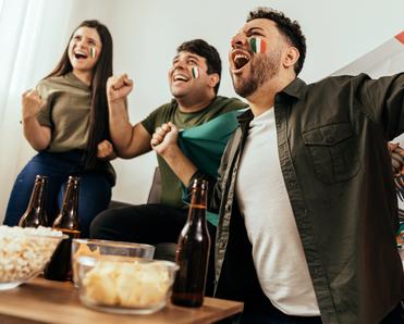 Two men and a woman with face paint and a Mexican flag cheering with beer and popcorn in the living room