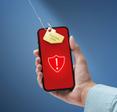 Hand holding phone with with shield and exclamation points on red screen a tag saying &quot;personal data&quot; is under a fishing hook trying to be pulled